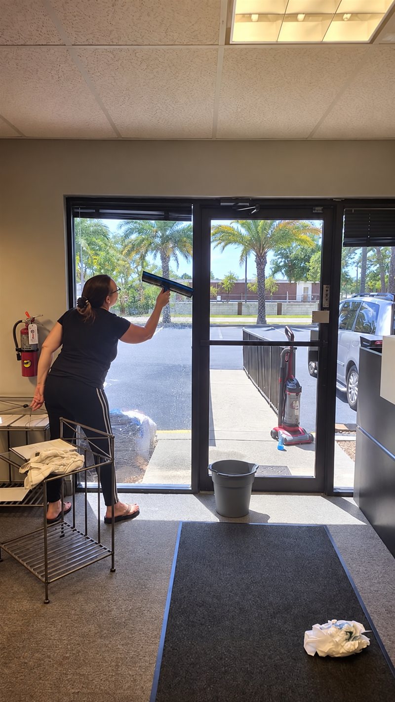 Nada's Cleaning team member cleaning a glass entry door